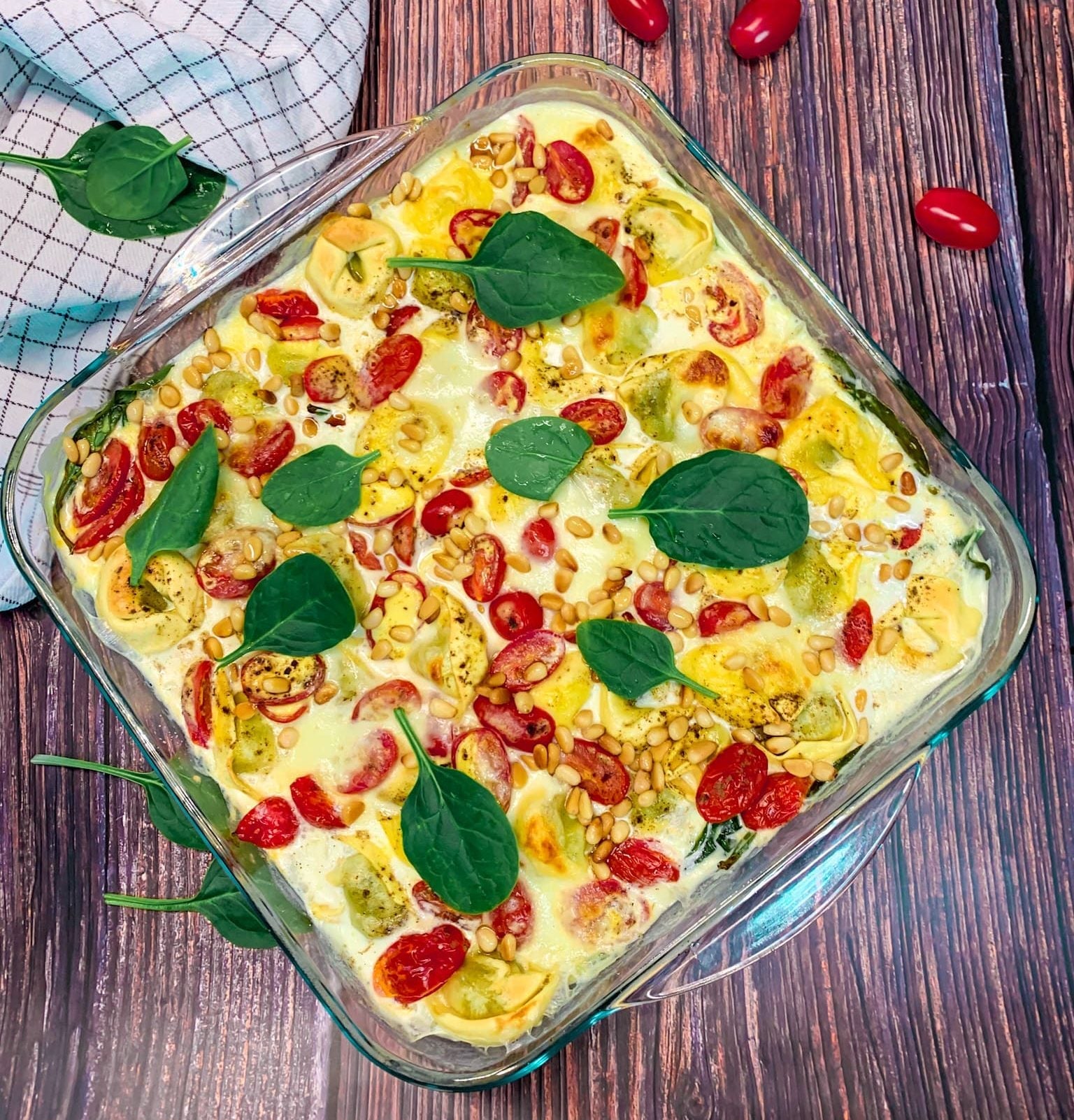 Goldbraun überbackener Tortelloniauflauf mit Cherrytomaten, Spinat, Mozzarella und Pinienkernen in einer Glasauflaufform