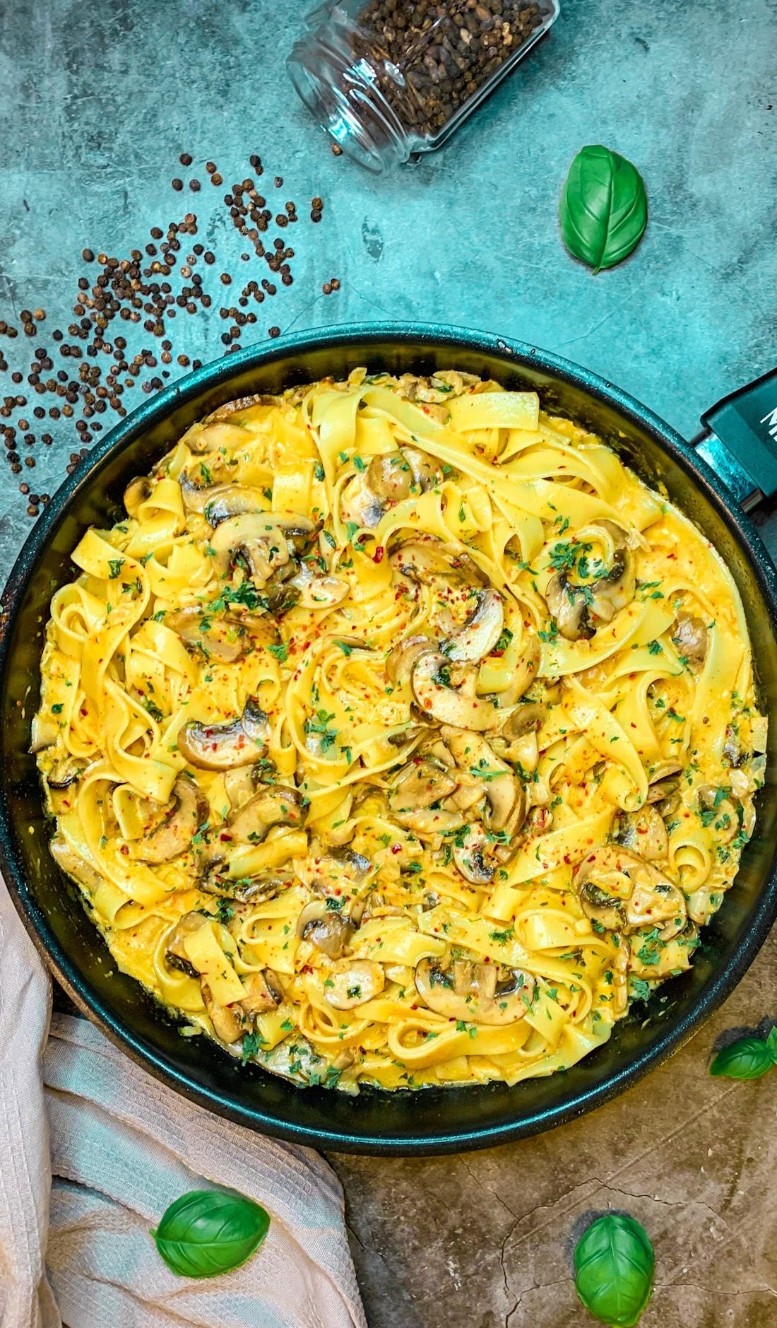 **Recipe Image Alt Text:**Cremige Champignonpasta mit Bandnudeln, frischen Champignons, Petersilie und einer würzigen Sahnesoße, serviert in einer schwarzen Pfanne, garniert mit Chiliflocken und frischem Basilikum.