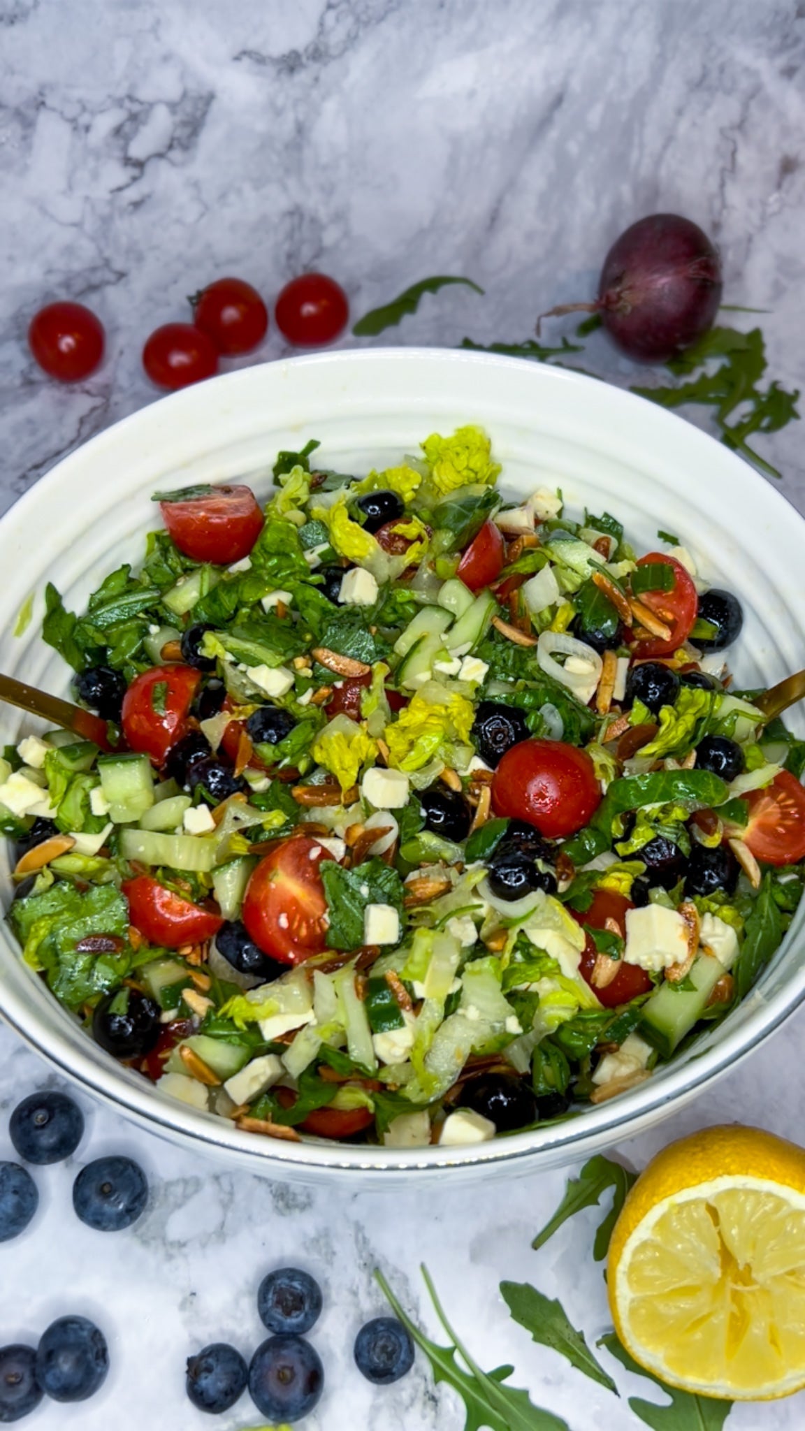 Frischer Salat mit Blaubeeren, Cherrytomaten, Gurke, Feta und Rucola, garniert mit gerösteten Mandeln und einem Honig-Granatapfelsirup-Dressing.