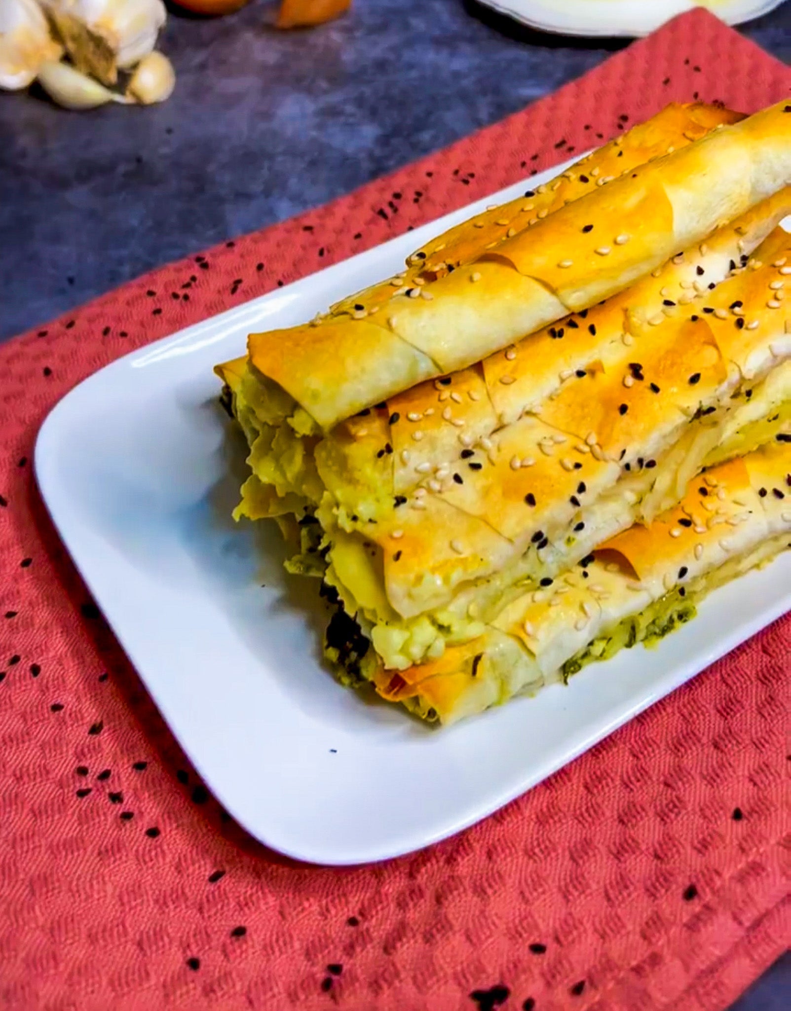 Knusprige Zigarren Börek gefüllt mit Spinat und Schafskäse, serviert auf einem Teller, garniert mit Sesam und Schwarzkümmel.