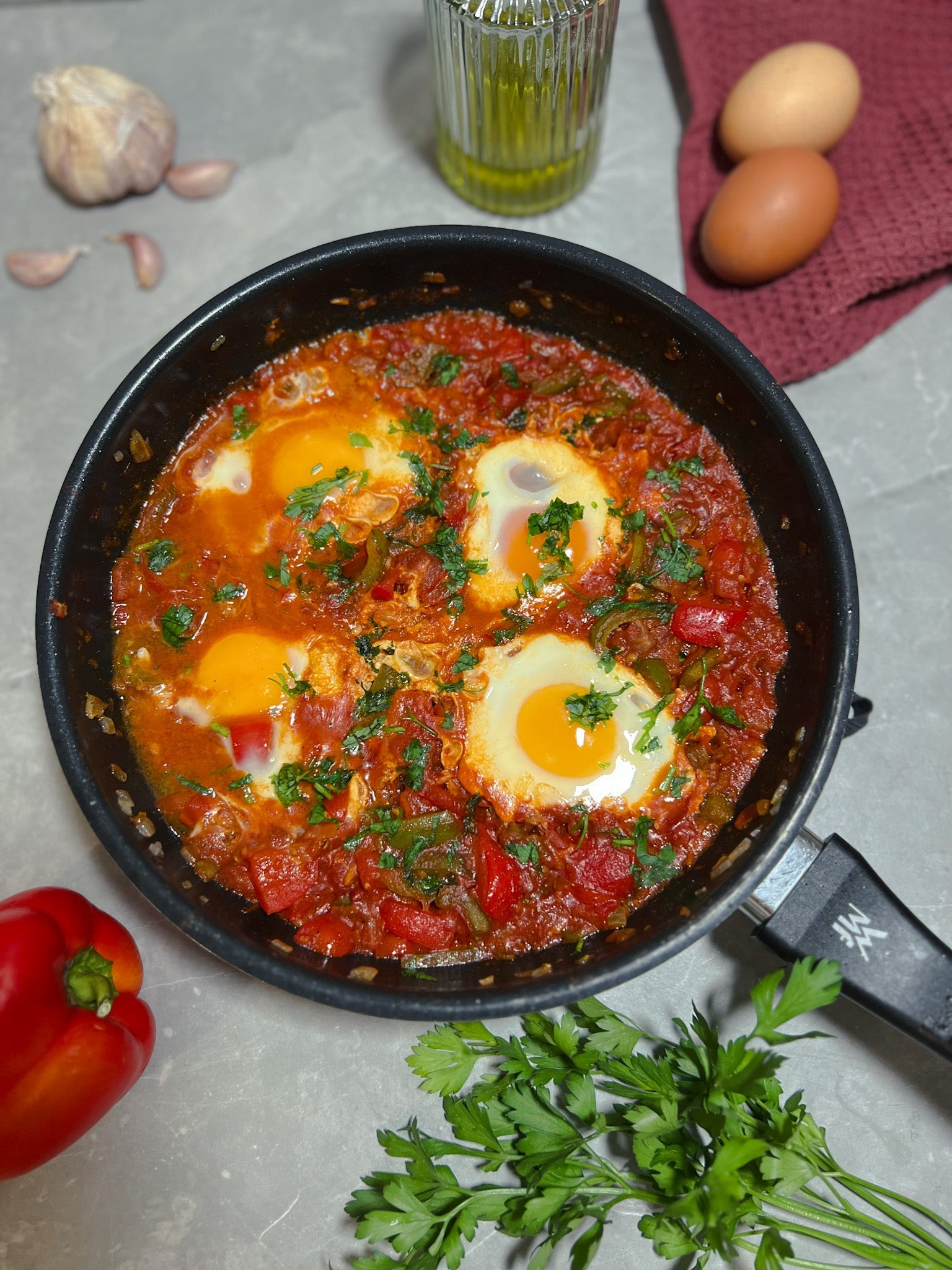 Shakshuka in einer Pfanne, serviert mit Fladenbrot und bestreut mit Paprikaflocken.