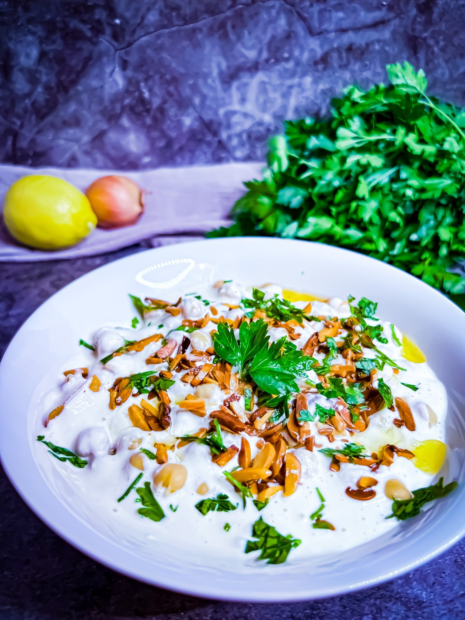 Vegetarische Fatteh mit Kichererbsen, Joghurtsoße, knusprigem Brot und gerösteten Mandeln, garniert mit frischer Petersilie.