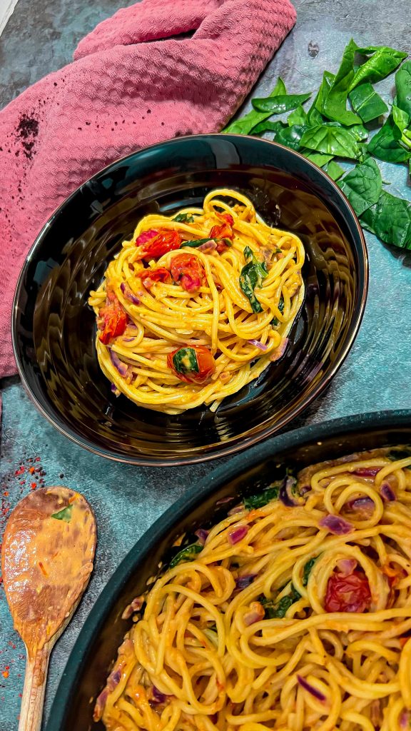 Ein Teller Spaghetti mit gerösteten Cherrytomaten und cremiger Knoblauchsoße, garniert mit frischem Spinat.