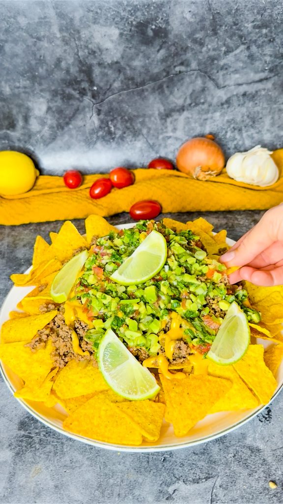 Nachos mit Hackfleisch, Käsesoße und Salsa, serviert auf einem großen Teller mit Koriander und Zitronenscheiben.