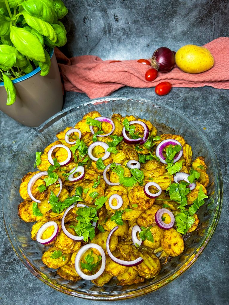 Goldbraune Tikka Masala Ofenkartoffeln, serviert mit frischem Koriander und roten Zwiebelringen.