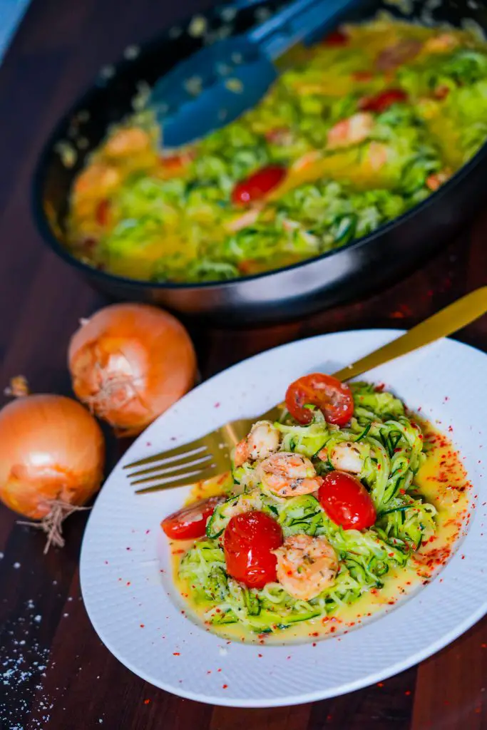 Ein Teller mit Zoodles, Garnelen und einer cremigen Soße, garniert mit Cherrytomaten und Parmesan.