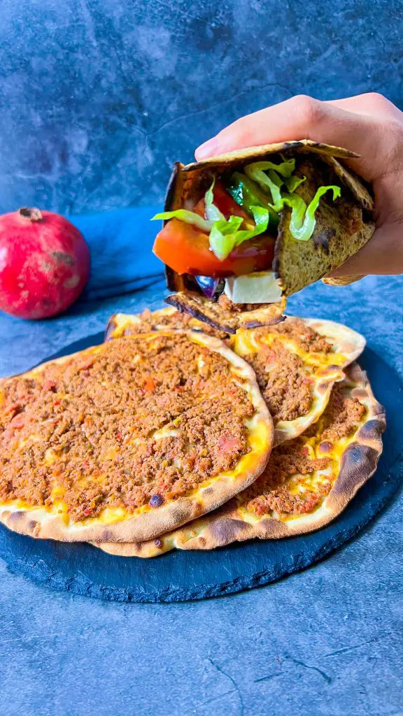 Ein köstlicher Lahmacun-Fladen, belegt mit Salat, Tomaten, Zwiebeln und Feta, daneben Tzaziki als Dip.